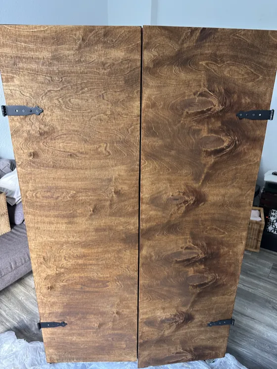 A tall wooden cupboard with two stained plywood doors and black hinges